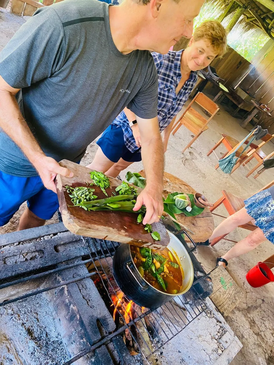 Guests adding fresh herbs to a pot cooking over an open fire